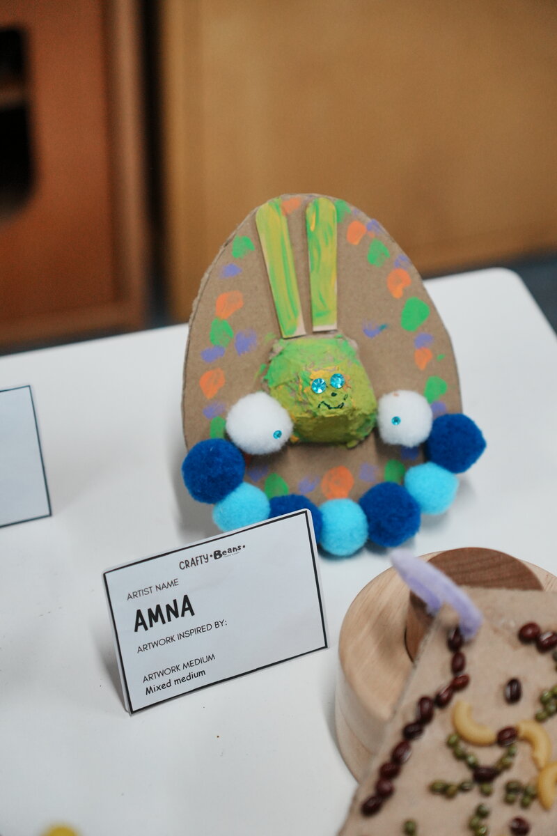 A child's mixed medium craft artwork on display with an artist name card