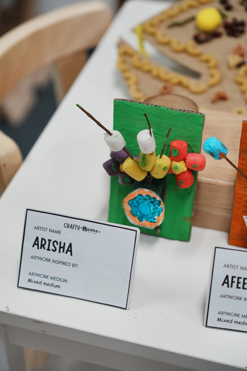 A child's mixed medium craft artwork on display with an artist name card