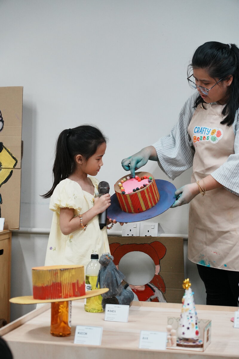 A child presenting her craft cake creation with a facilitator