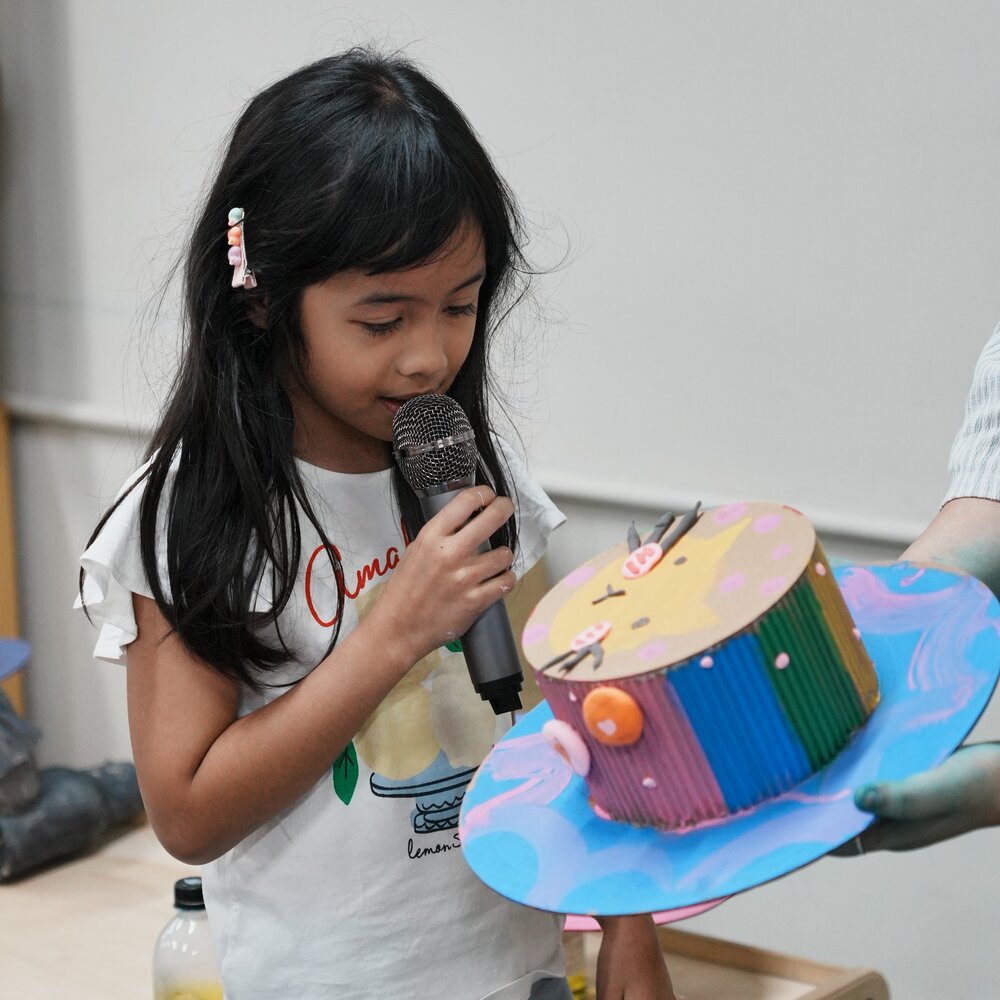 A child speaking into a microphone about her craft cake