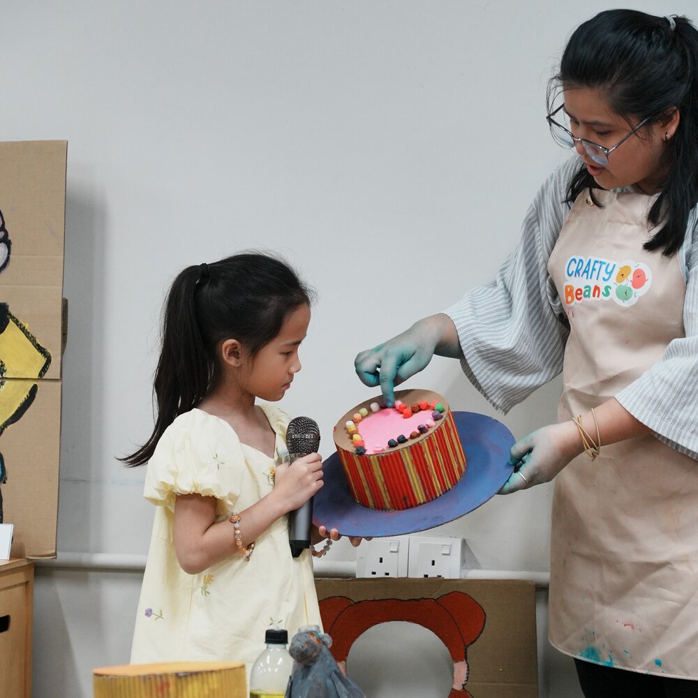A facilitator helping a child present her craft cake