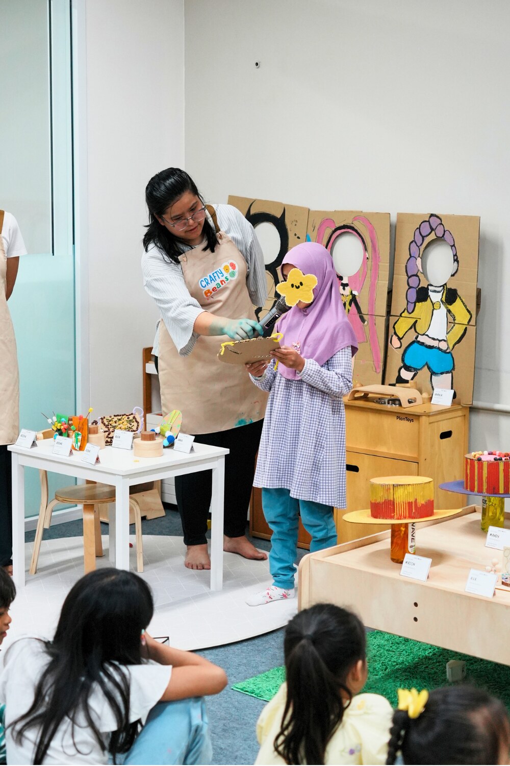 A facilitator helping a child present her craft artwork