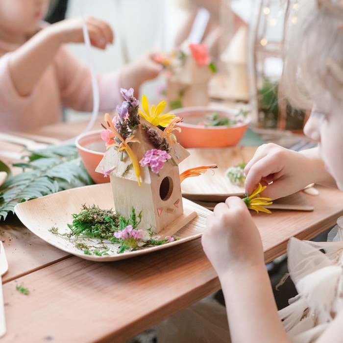 Children decorating a birdhouse craft with flowers under guidance